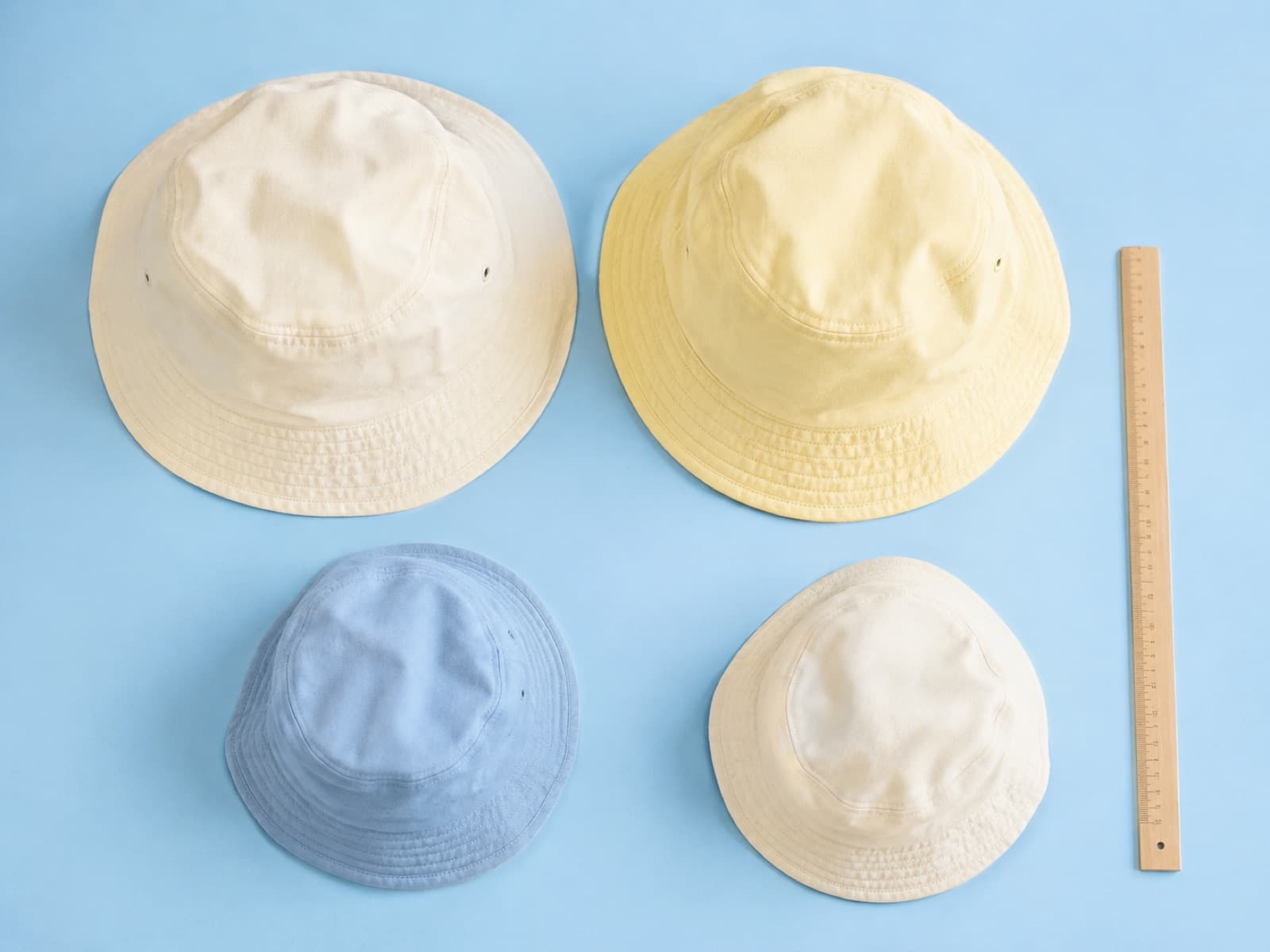 Four soft bucket hats in graduated sizes laid out together on a sky-blue surface